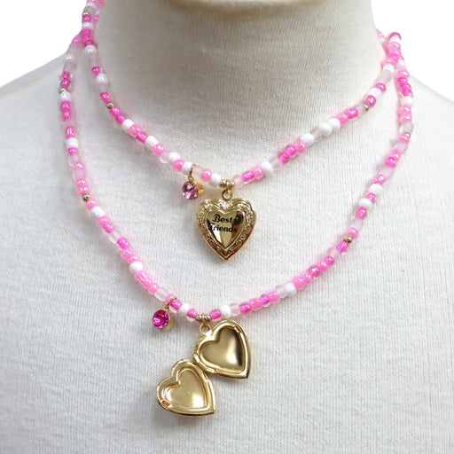 Two gold heart-shaped best friends pendants on pink beaded necklaces against a white background