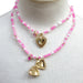 Two gold heart-shaped best friends pendants on pink beaded necklaces against a white background
